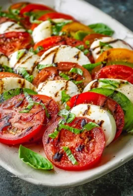 Fresh Caprese Salad with tomatoes, mozzarella, and basil on a white plate.
