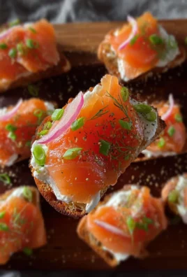 Smoked salmon crostini topped with cream cheese and herbs on a wooden board.