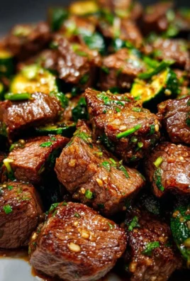 Garlic butter steak bites served sizzling on a plate with herbs and spices.