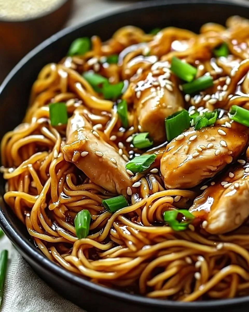 Plate of sticky garlic chicken noodles garnished with herbs