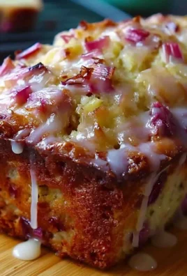 Lemon rhubarb loaf with glaze on a plate, garnished with lemon slices.