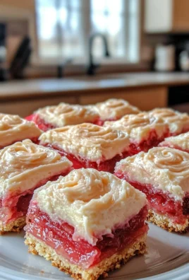 Delicious rhubarb bars topped with cream cheese frosting on a wooden table.