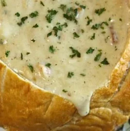 Bowl of chunky New England clam chowder topped with herbs and crackers
