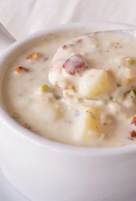 Bowl of New England clam chowder garnished with parsley and served with crackers.