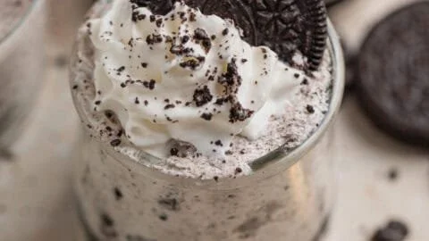 Delicious Oreo no-bake cheesecake cups garnished with whipped cream and Oreo crumbs.