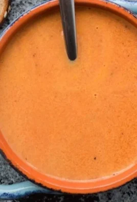 A bowl of creamy tomato soup garnished with fresh basil and cream.