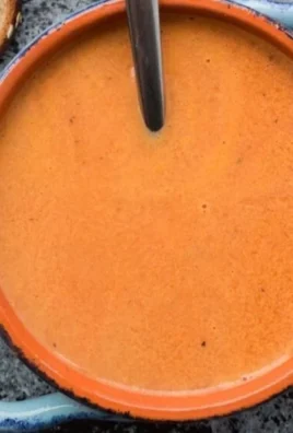 Bowl of creamy tomato soup topped with fresh basil and a swirl of cream.
