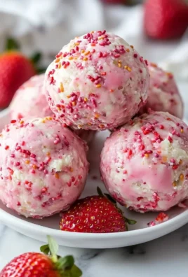 Strawberry cheesecake protein balls on a white plate with fresh strawberries.